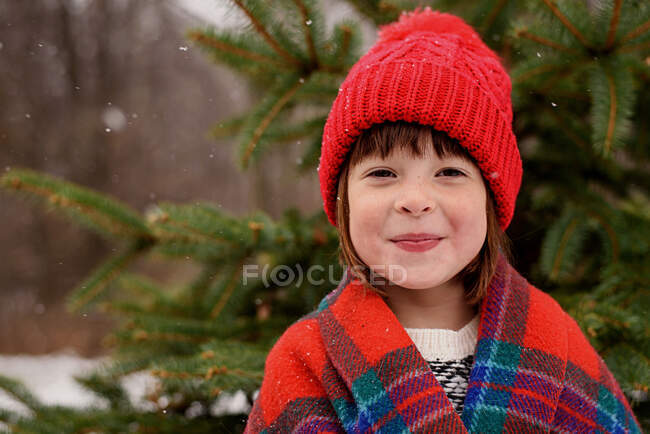 Portrait d'une fille enveloppée dans une couverture debout devant un sapin de Noël — Photo de stock