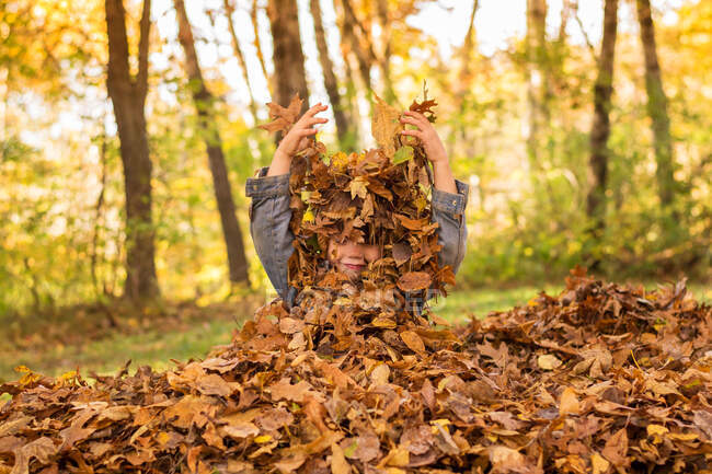 Ragazzo nascosto in foglie autunnali sulla natura — Foto stock
