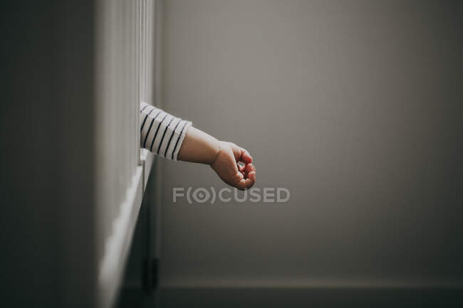 Baby boy's hand hanging out of cot — Stock Photo