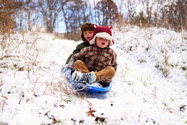 Two children sledding down hill in the snow — Stock Photo