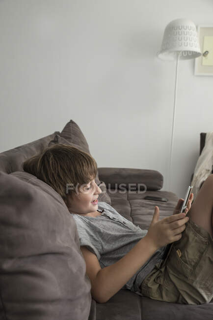 Хлопчик сидить на дивані зі своїм цифровим планшетом — стокове фото
