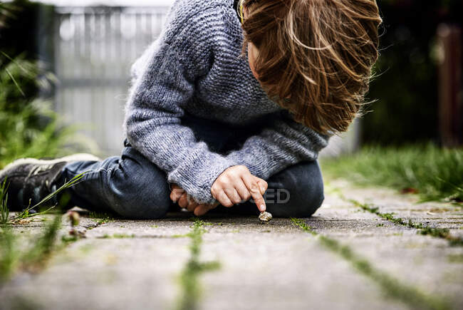 Хлопчик сидить на землі дивлячись на равлика — стокове фото