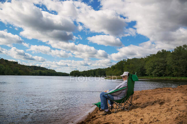 Homem sênior sentado à beira da pesca fluvial — Fotografia de Stock