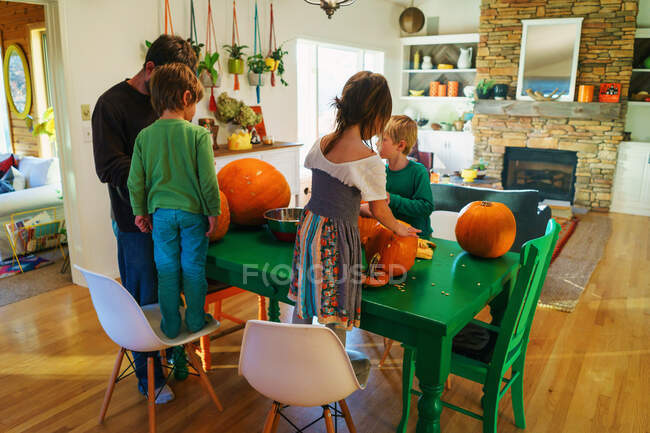 Pai e três crianças preparando abóboras na cozinha — Fotografia de Stock