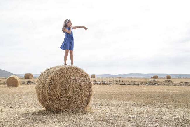 Menina de pé em um fardo de feno em um campo — Fotografia de Stock