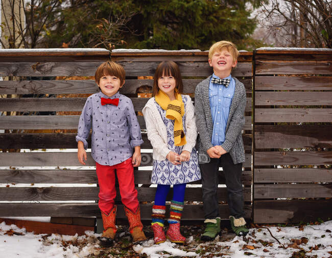 Tres niños felices de pie junto a una valla en el jardín - foto de stock