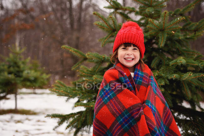 Retrato de uma menina envolto em um cobertor de pé na frente de uma árvore de Natal — Fotografia de Stock
