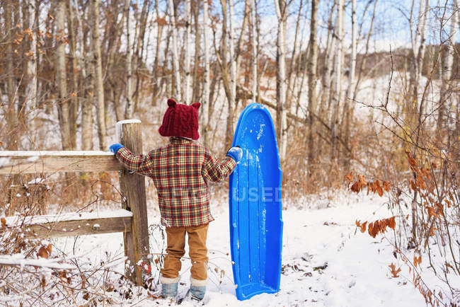 Menino de pé na neve segurando um trenó — Fotografia de Stock