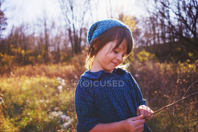 Chica de pie en un prado sosteniendo una rama - foto de stock