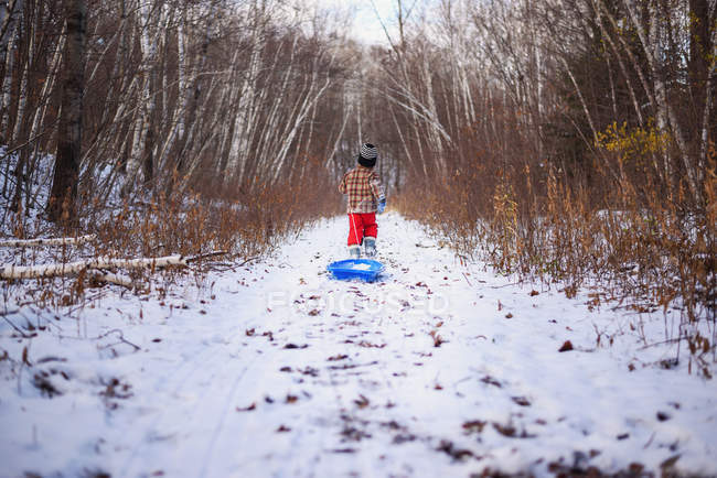 Junge zieht seinen Schlitten auf Fußweg — Stockfoto