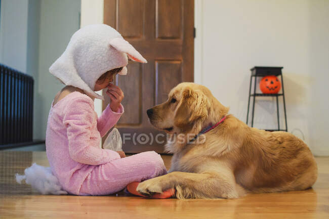 Fille en costume de lapin partage bonbons d'Halloween avec Golden Retriever chien — Photo de stock
