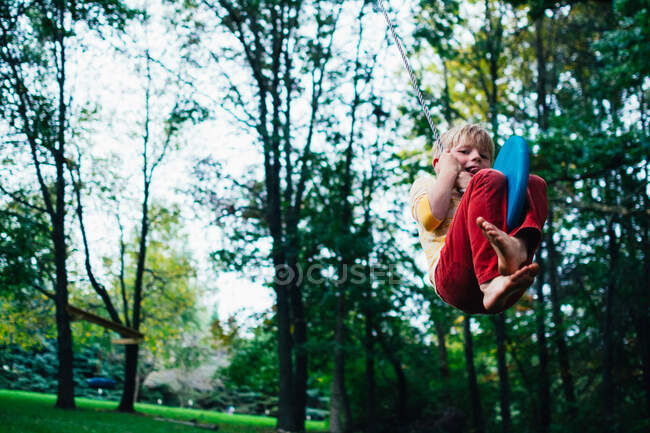Garçon balançant sur une balançoire de corde dans le jardin — Photo de stock