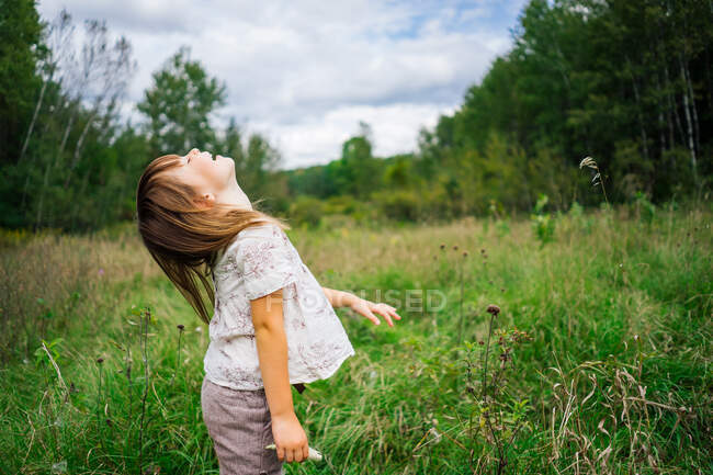 Chica de pie en el campo lanzando su cabeza hacia atrás riendo - foto de stock