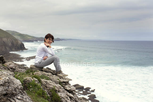 Retrato de uma mulher sorridente sentada sobre rochas junto ao mar, Santillana del Mar, Cantábria, Espanha — Fotografia de Stock
