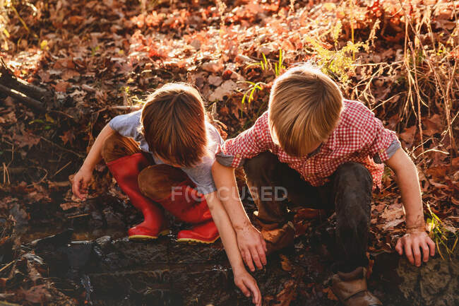 Two boys playing in mud by a river — Stock Photo