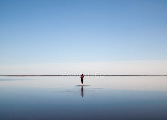 Vista trasera del hombre corriendo a lo largo de la playa de arenas rojas, Islandia - foto de stock