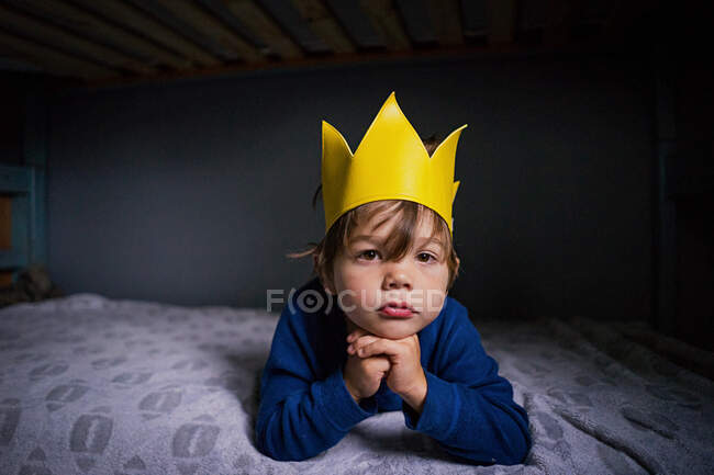 Портрет мальчика в короне, лежащего на кровати — стоковое фото