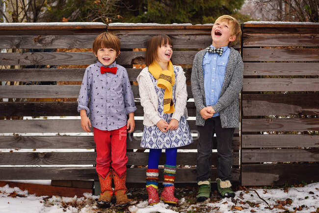 Três crianças felizes em pé junto a uma cerca no jardim — Fotografia de Stock