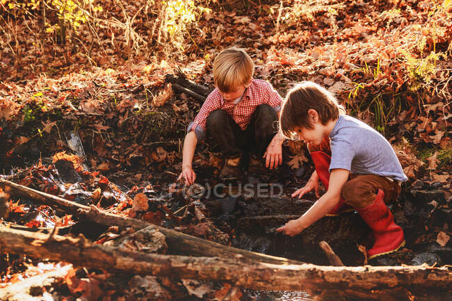 Dos chicos jugando en el barro junto a un río - foto de stock