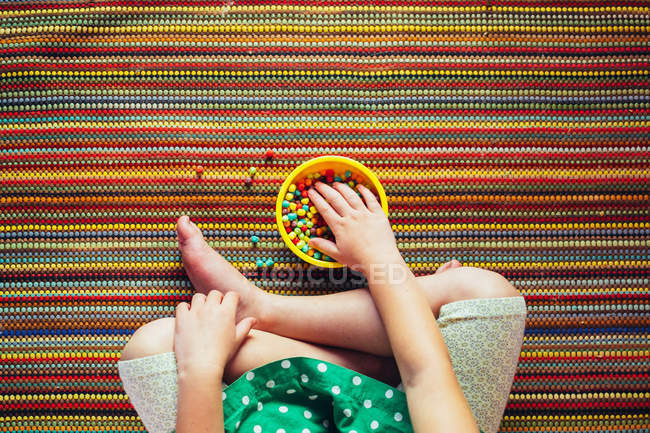 Cropped image of Girl sitting cross legged eating multi-colored snacks — Stock Photo