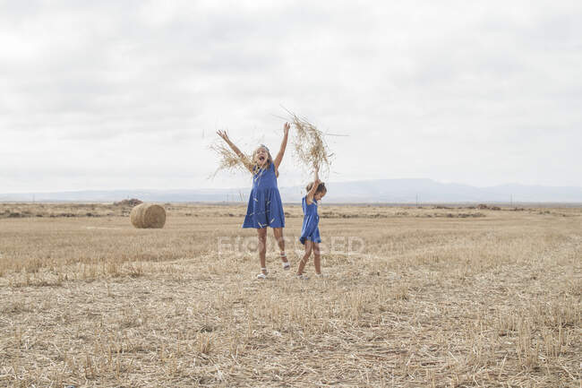 Two girls in a field throwing staw in the air — Stock Photo