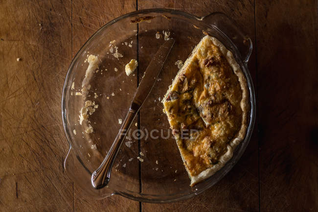 Half eaten quiche in a glass bowl with a knife — Stock Photo