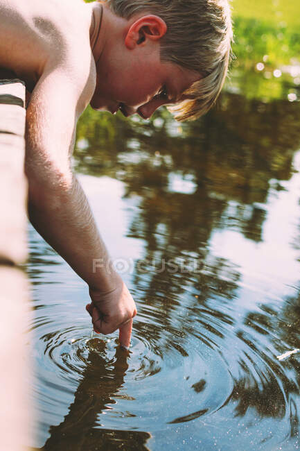 Menino pendurado sobre doca tocando a água — Fotografia de Stock