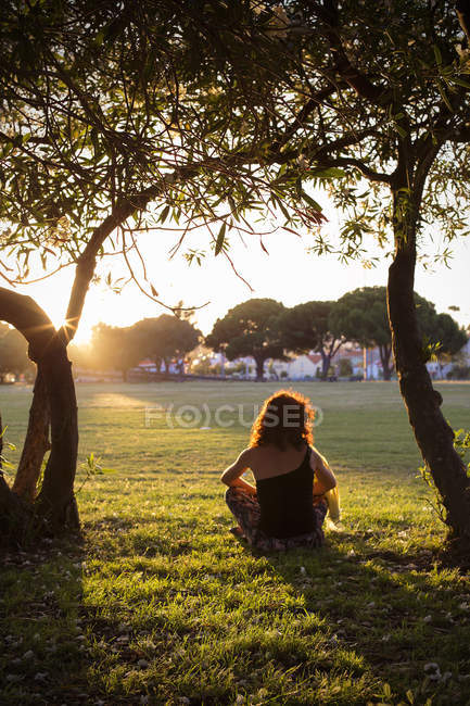 Женщина сидит в парке на закате, Лиссабон, Португалия — стоковое фото