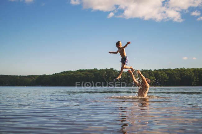 Батько кидає сина в повітря, стоячи в озері — стокове фото