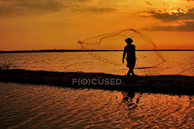 Silhouette d'un pêcheur jetant son filet, Banjarbaru, Kalimantan du Sud, Indonésie — Photo de stock