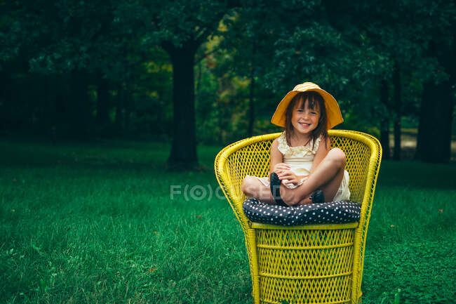 Портрет улыбающейся девушки, сидящей в садовом кресле — стоковое фото