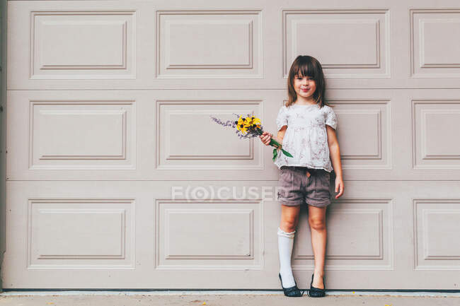 Fille debout devant la porte de garage tenant des fleurs — Photo de stock