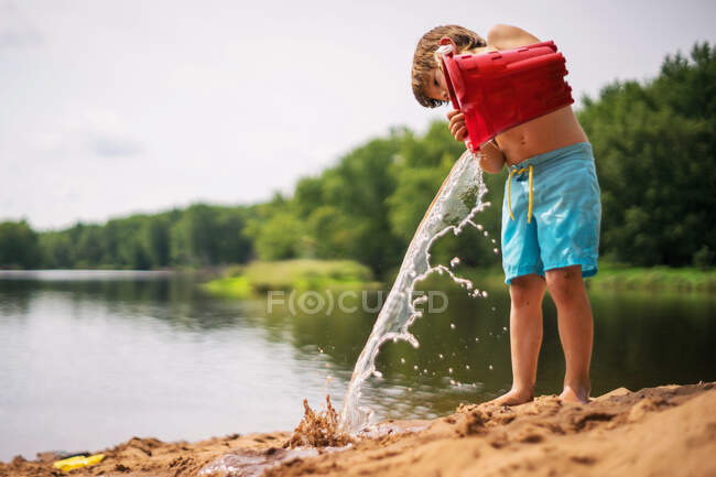 Chico vaciando un cubo de agua en la playa - foto de stock