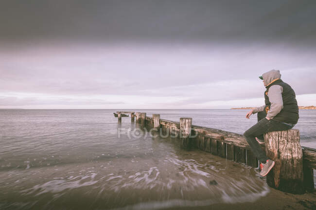 Мужчина, сидящий на деревянной канавке на пляже, Мельбурн, штат Виктория, Австралия — стоковое фото
