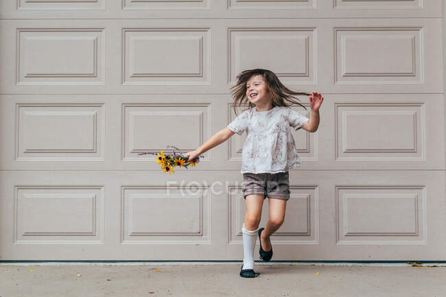 Menina de pé na frente da porta da garagem segurando flores — Fotografia de Stock