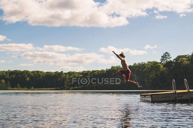 Uomo che salta dal molo in un lago — Foto stock