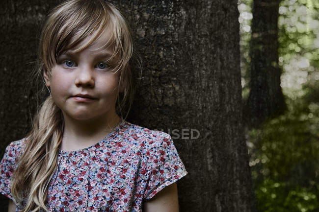 Retrato de una niña de pie junto a un árbol - foto de stock
