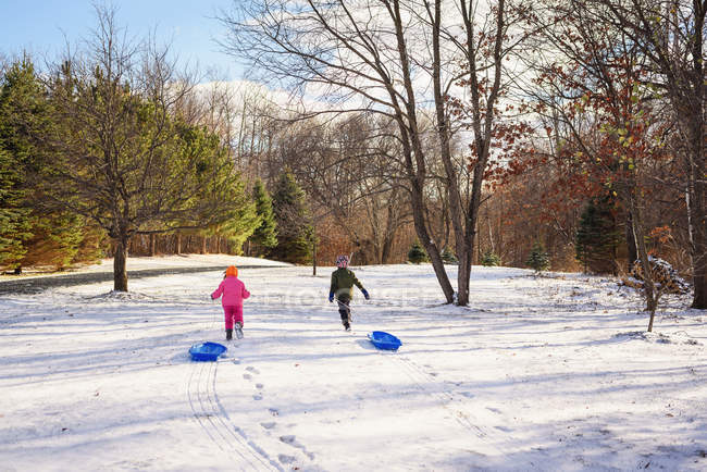 Duas crianças puxando trenós através da neve — Fotografia de Stock