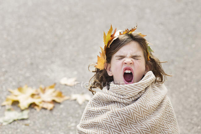 Chica envuelta en una manta con una corona de hojas en su pelo bostezando - foto de stock