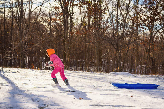 Chica tirando de su trineo a través de la nieve - foto de stock