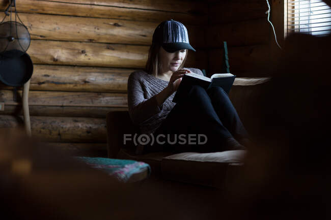 Женщина, читающая книгу в бревенчатой хижине — стоковое фото