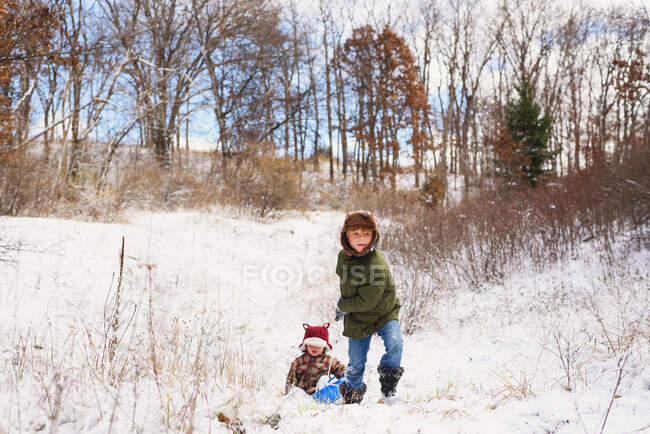 Мальчик тащит брата на санях в снегу — стоковое фото
