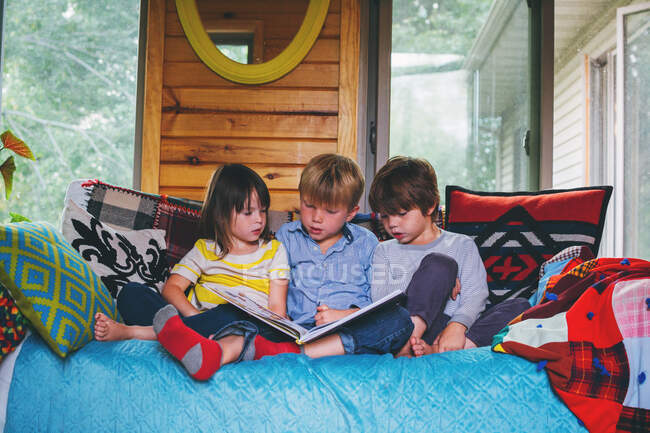 Three children sitting on couch reading — Stock Photo