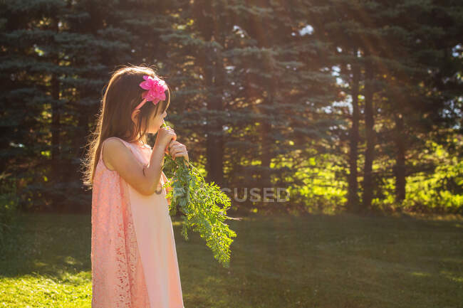 Mädchen steht im Garten und isst eine frisch gepflückte Möhre — Stockfoto