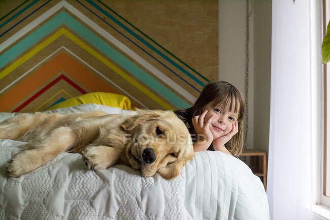 Girl and golden retriever dog lying on bed — Stock Photo