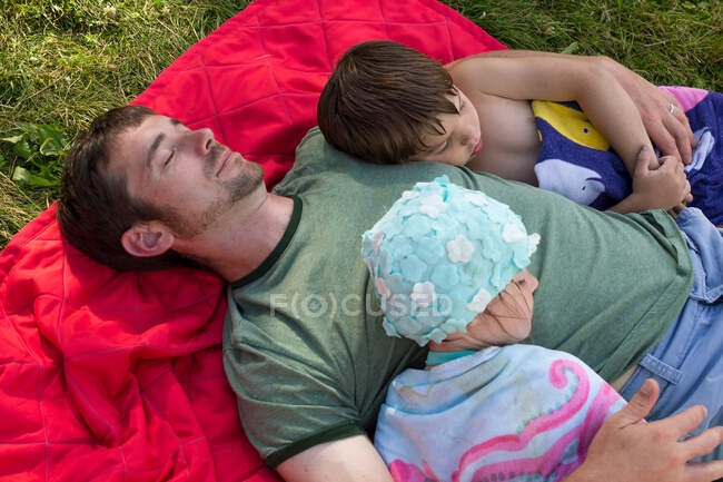 Père et deux enfants dorment sur une couverture de pique-nique — Photo de stock