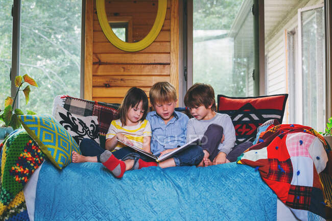 Tres niños sentados en el sofá leyendo - foto de stock