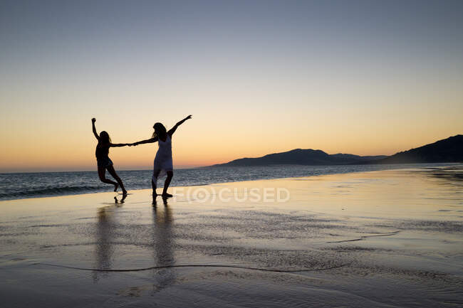 Silhueta de duas mulheres dançando na praia de Los Lances ao pôr do sol, Tarifa, Cádiz, Andaluzia, Espanha — Fotografia de Stock