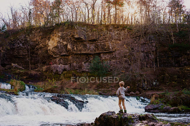 Niño lanzando piedras en una cascada - foto de stock