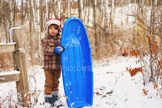 Хлопчик стоїть у снігу, тримаючи сани. — стокове фото